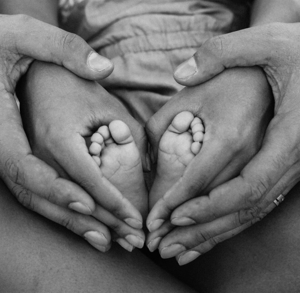 Black and white photo of adult hands cradling baby feet, symbolizing family love and connection.